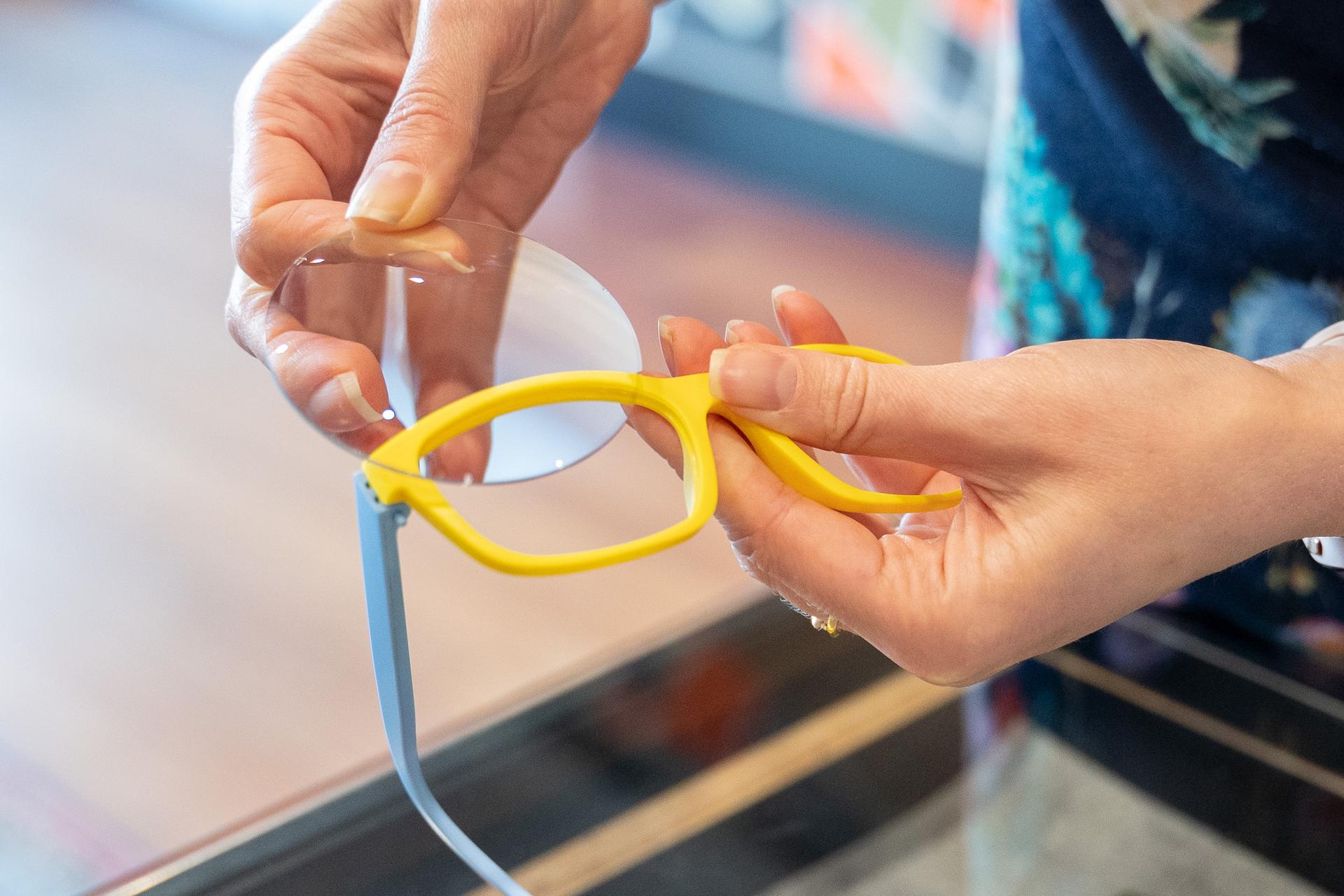 Close up of a person fitting a prescription lens into a yellow Dresden Vision New Zealand frame, highlighting modular eyewear options.