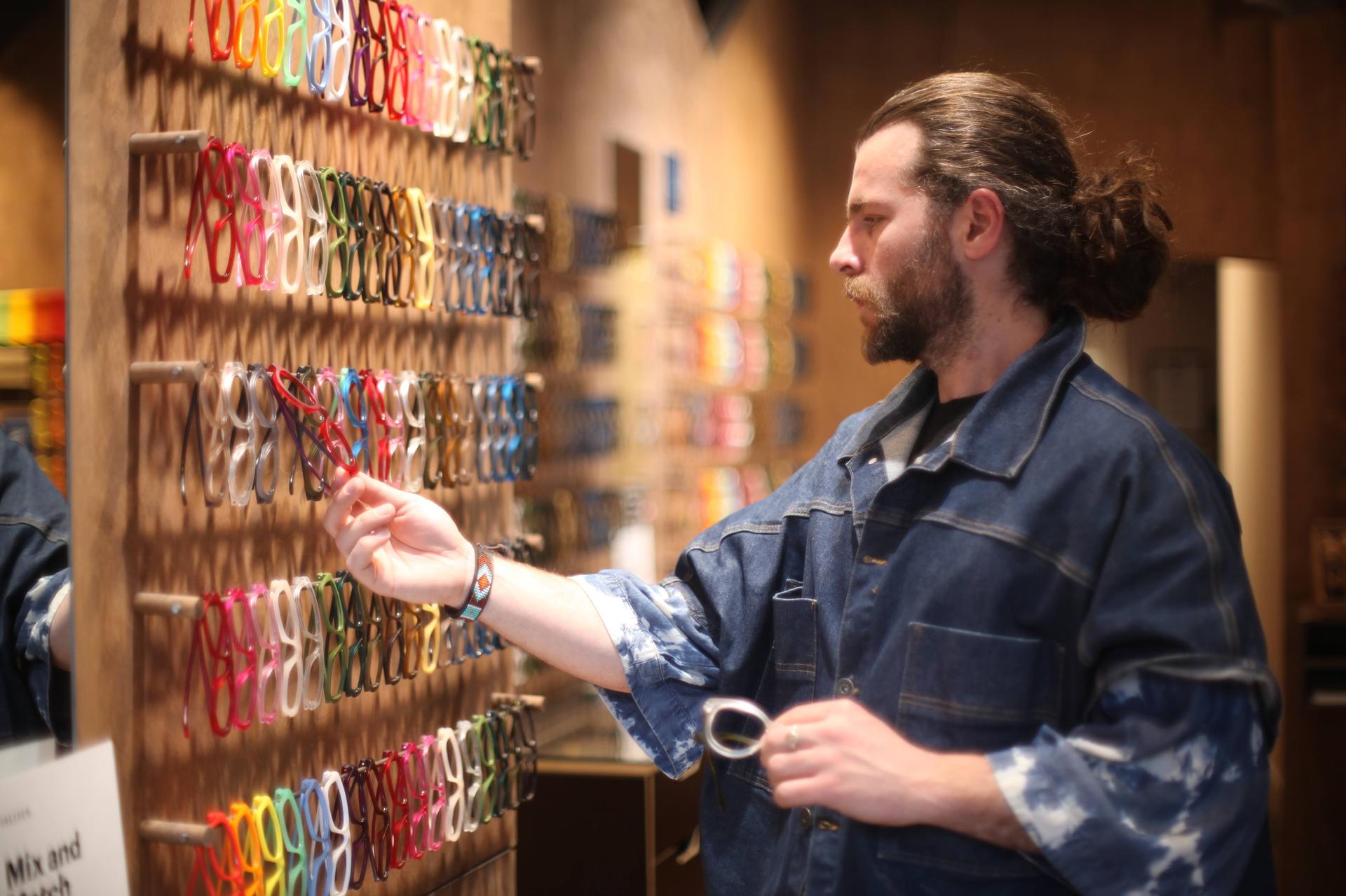 A customer browses a colourful wall of Dresden Vision Australias interchangeable eyewear frames, exploring affordable Black Friday prescription glasses options.
