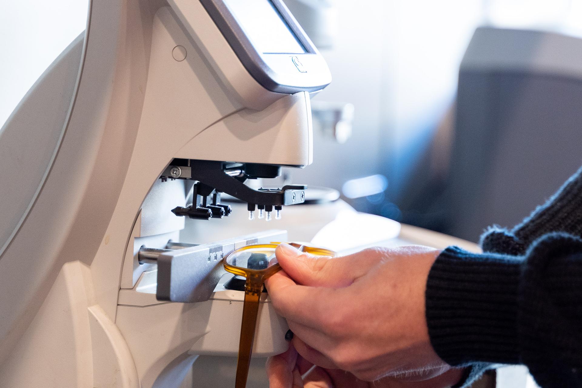 Hands adjusting glasses under a lens verification device at Dresden Vision Canada, reflecting the steps required to turn eye exam prescriptions into same day glasses.