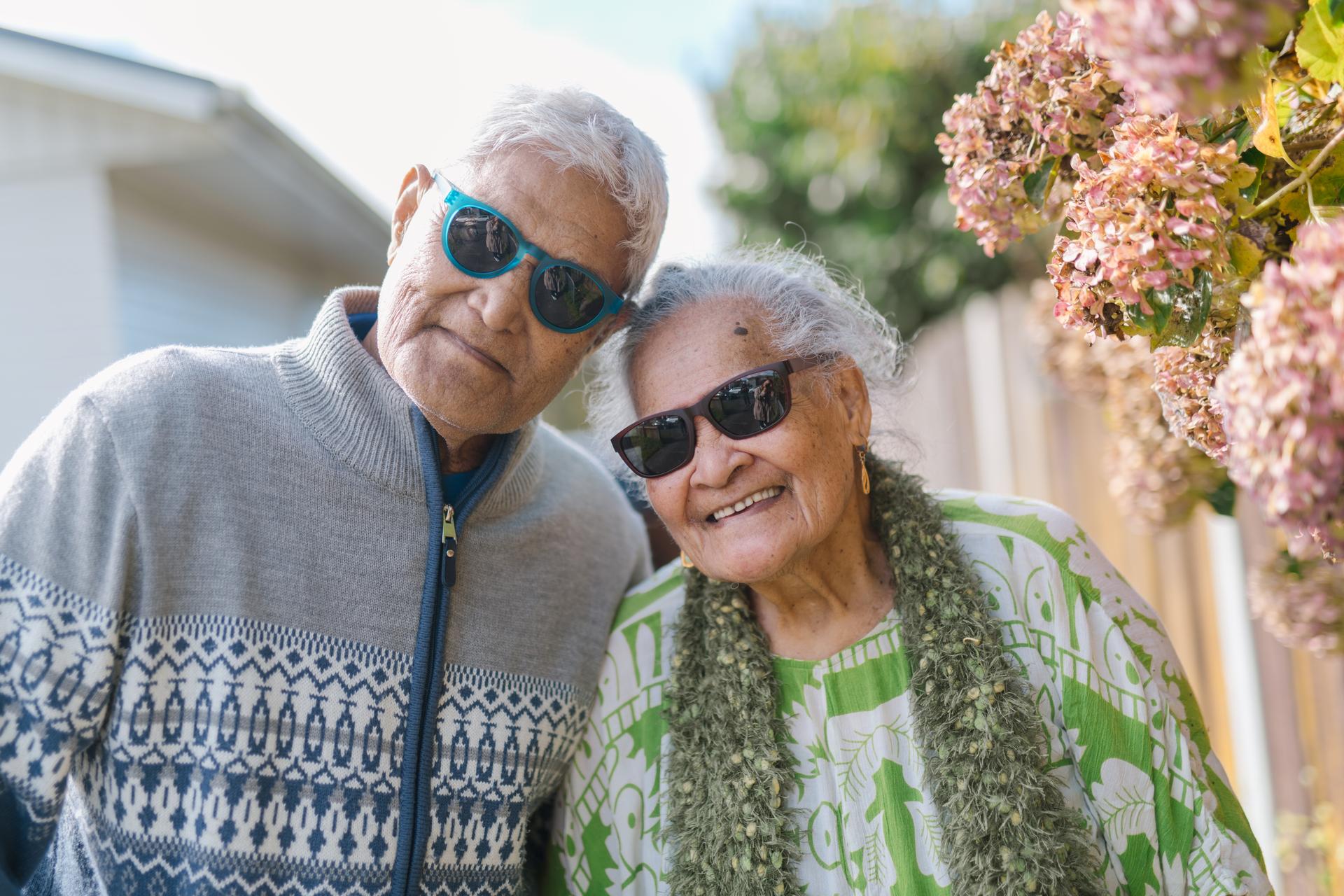 A smiling elderly man in blue sunglasses leans towards a cheerful woman in black sunnies—both wearing Dresden Vision United States prescription sunglasses for sun protection.