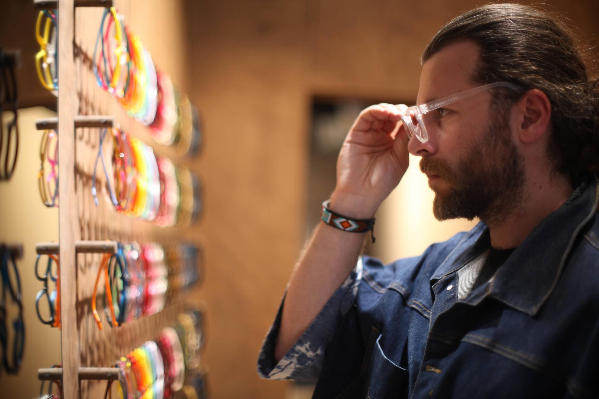 In a Dresden Vision United States setting, a man evaluates multifocal glasses beside a display of sustainable frames showing the importance of a customised multifocal lens fitting experience.