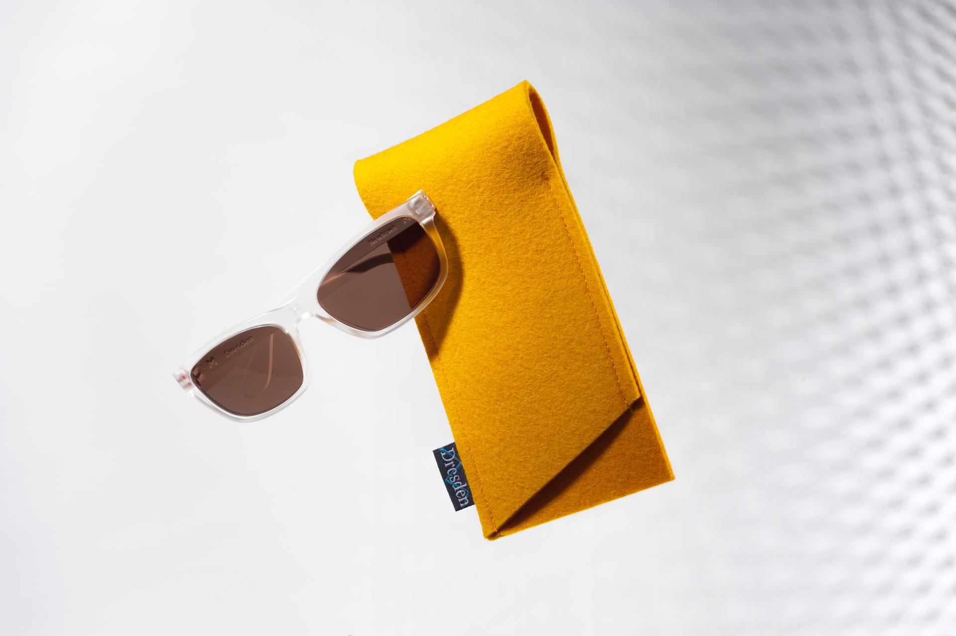Clear-framed Dresden Vision Australia sunglasses with brown lenses and their yellow case, addressing the importance of verifying frame authenticity and UV protection when buying sunnies online in Australia.
