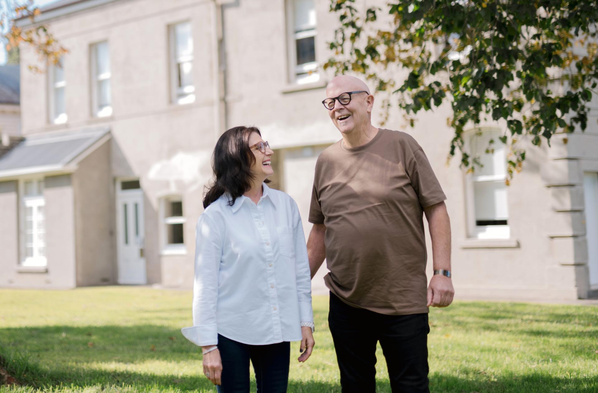 Smiling couple with modern prescription glasses from Dresden Vision United States, standing outside a bright and airy home.