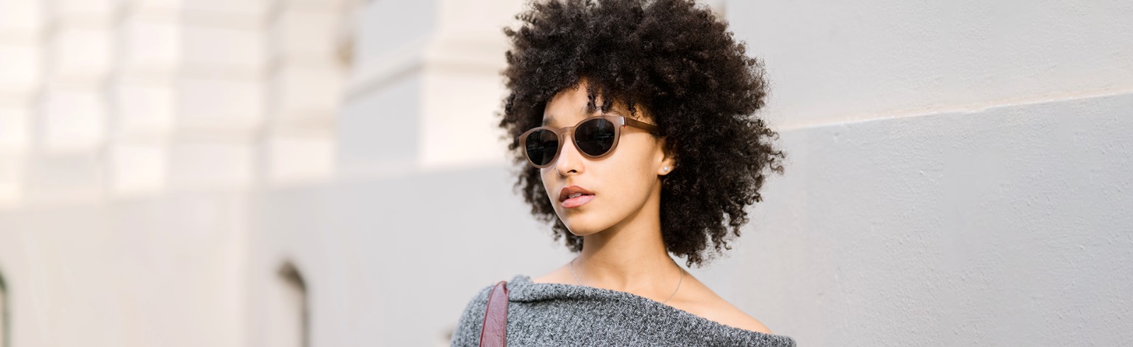 Dresden Vision sunglasses offer versatile style for any occasion. A person with curly hair confidently wears our brown-framed sunglasses and a grey top, representing modern Canadian fashion.