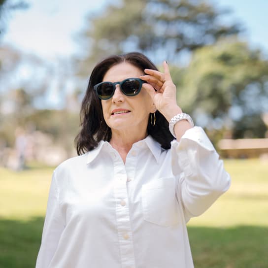 Elegant woman in polarised sunglasses in Canada, wearing a white shirt and watch, enjoying a bright day outdoors in a park setting with stylish eye protection.
