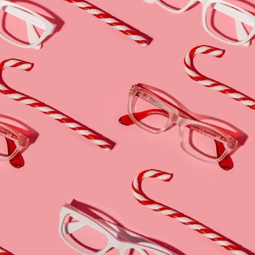 Red and white eyeglasses paired with diagonal red and white candy canes on a pink background create a festive arrangement representing Christmas glasses in New Zealand with a cheerful and colourful holiday-inspired design.