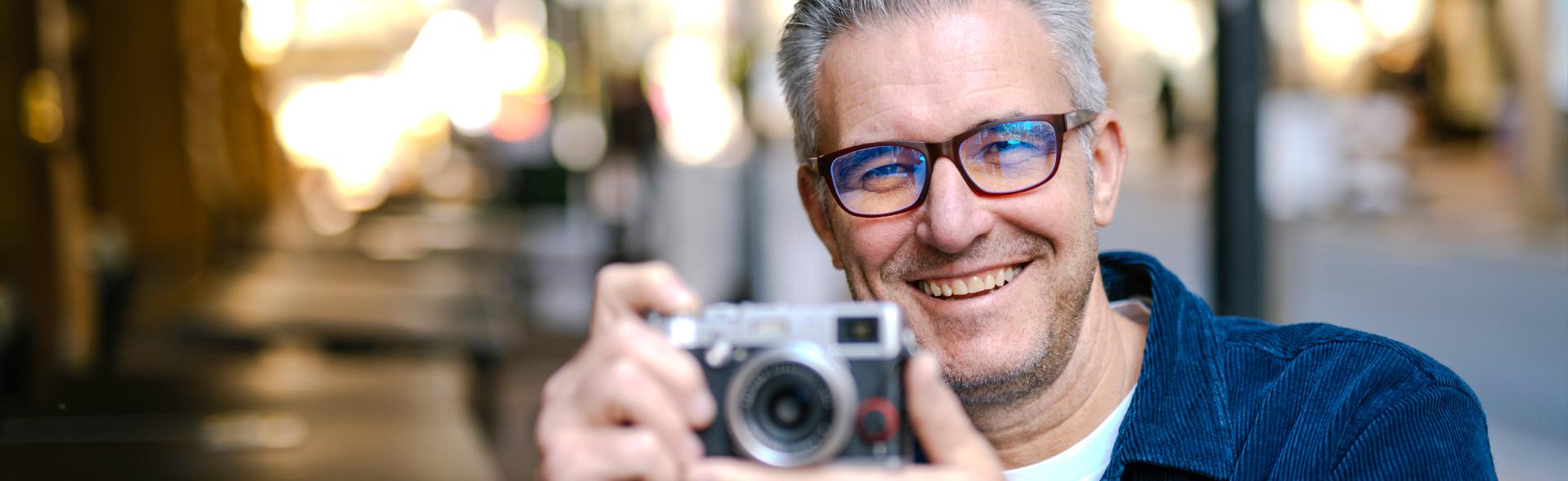 Smiling man wearing Dresden Vision New Zealand blue light filter glasses, with screen reflections visible on the lenses