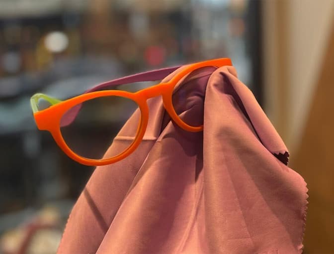 Bold orange Dresden Vision eyeglasses cleaned with a soft lens cloth, demonstrating reliable eyewear cleaning solutions for everyday use in Canada.