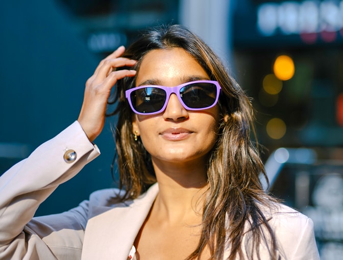 Woman wearing Dresden Vision Australia sunglasses in purple frames, adjusting her hair in a city at night