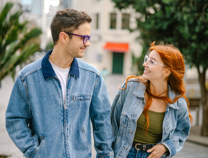 Couple wearing Dresden Vision Australia prescription glasses, smiling at each other outdoors, violet and clear frames