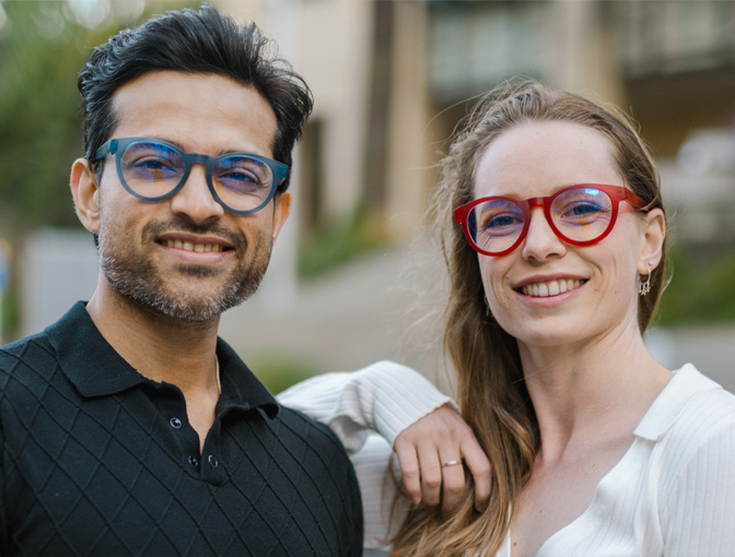 A man and woman wearing bold Dresden Vision Canada progressive glasses, highlighting the brand’s signature blue and red modular frames engineered for clear near, intermediate, and distance vision.