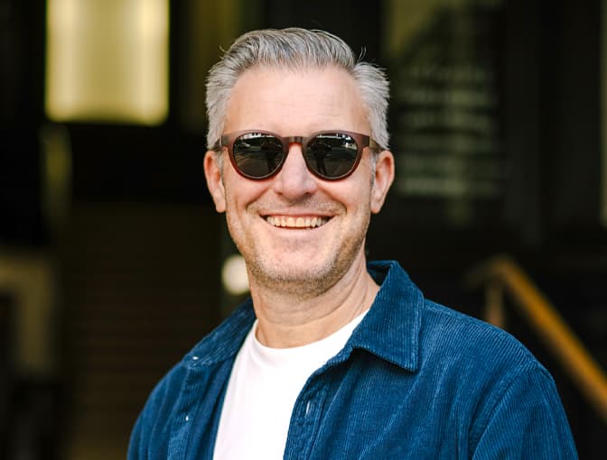 Man in Dresden Vision Canada progressive sunglasses, standing in front of an urban doorway with a relaxed expression