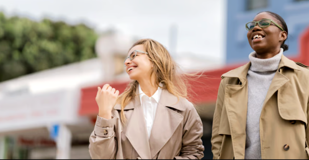 Two women walking outdoors, one wearing Dresden Vision Australia prescription glasses, smiling together in an urban setting.