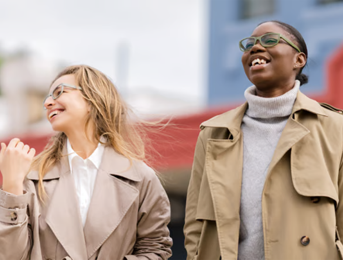 Two women walking outdoors, one wearing Dresden Vision Australia prescription glasses, smiling together in an urban setting.