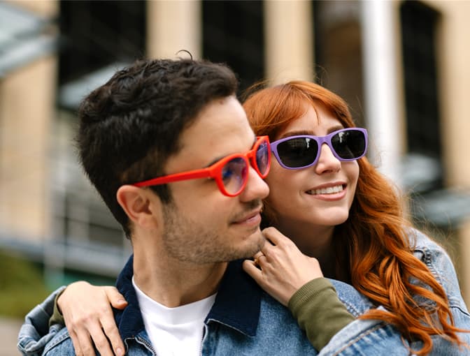 Couple wearing Dresden Vision glasses in colourful frames, posing together in a lifestyle city scene