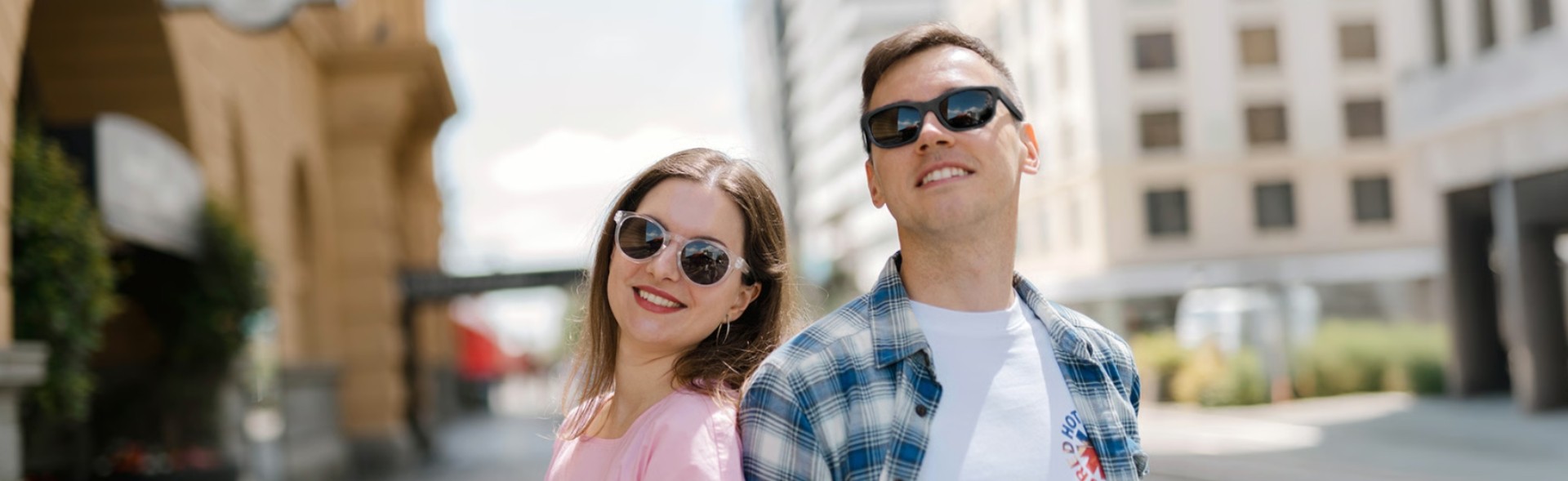 A man and a woman wearing sunglasses smiling outdoors in the city