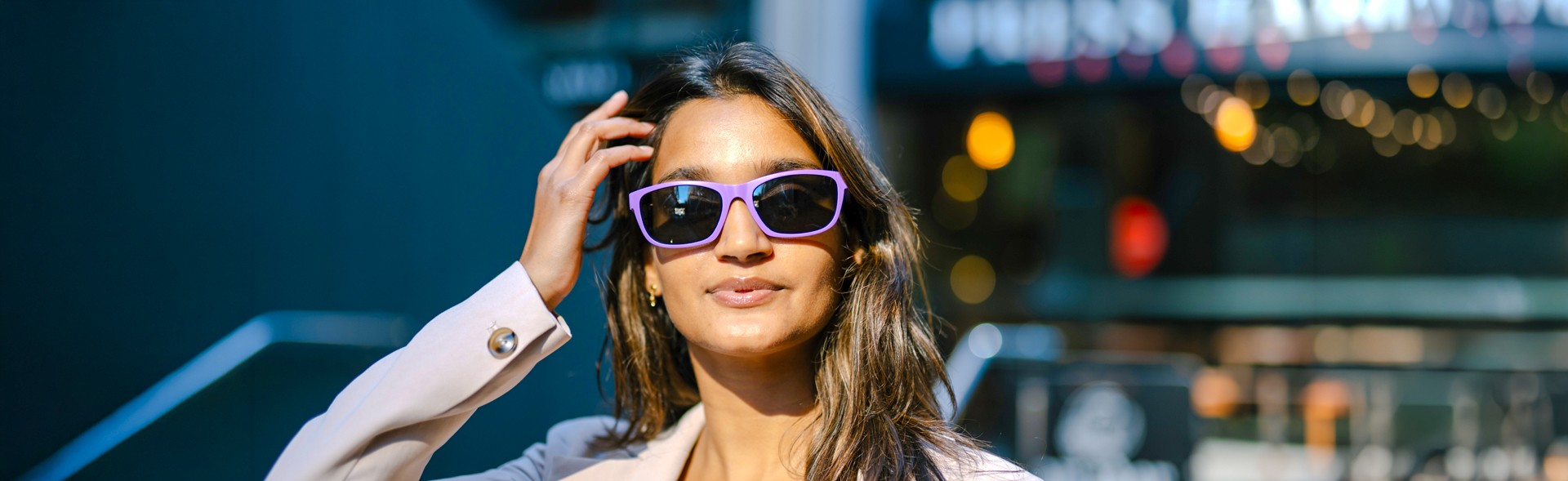 Woman wearing Dresden Vision Australia sunglasses in purple frames, adjusting her hair in a city at night