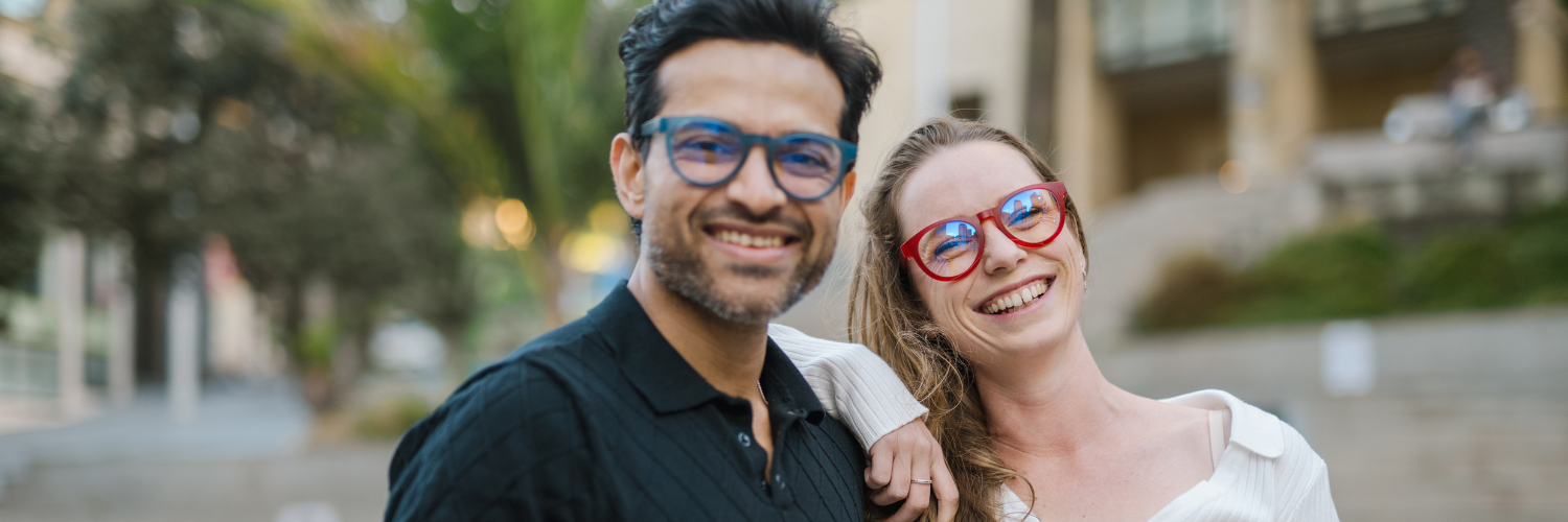 Happy pair wearing red and blue Dresden Vision Canada prescription glasses, enjoying a casual day out with relaxed, playful energy.
