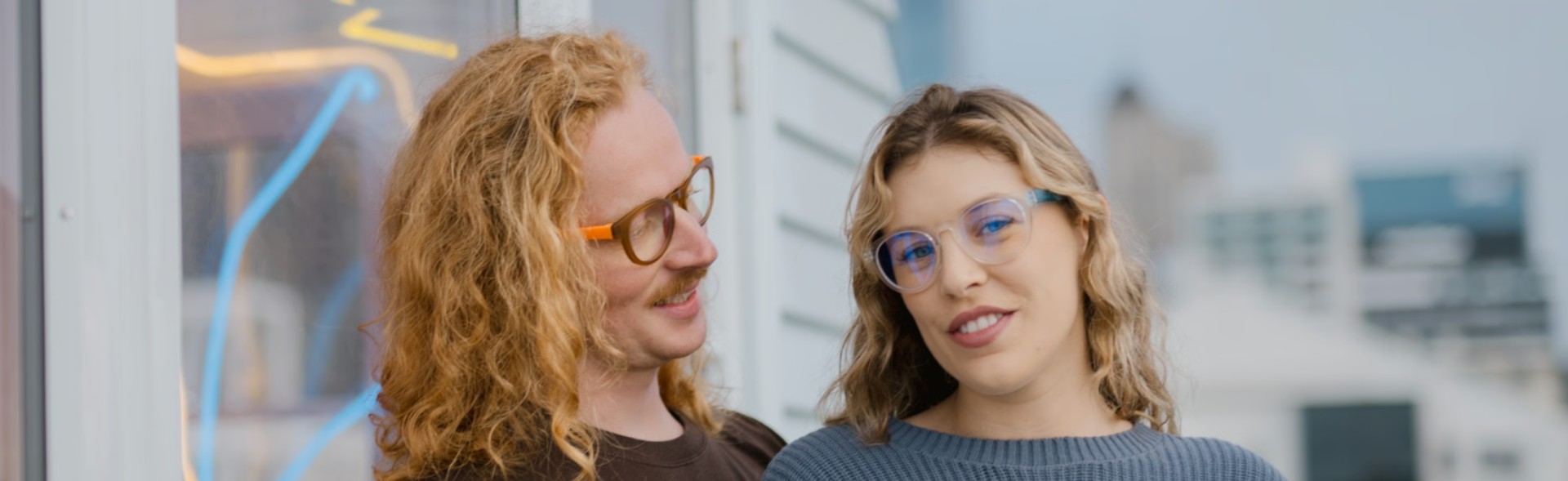 Couple wearing stylish prescription glasses in Australia, showcasing modern orange and clear blue frame designs outdoors.