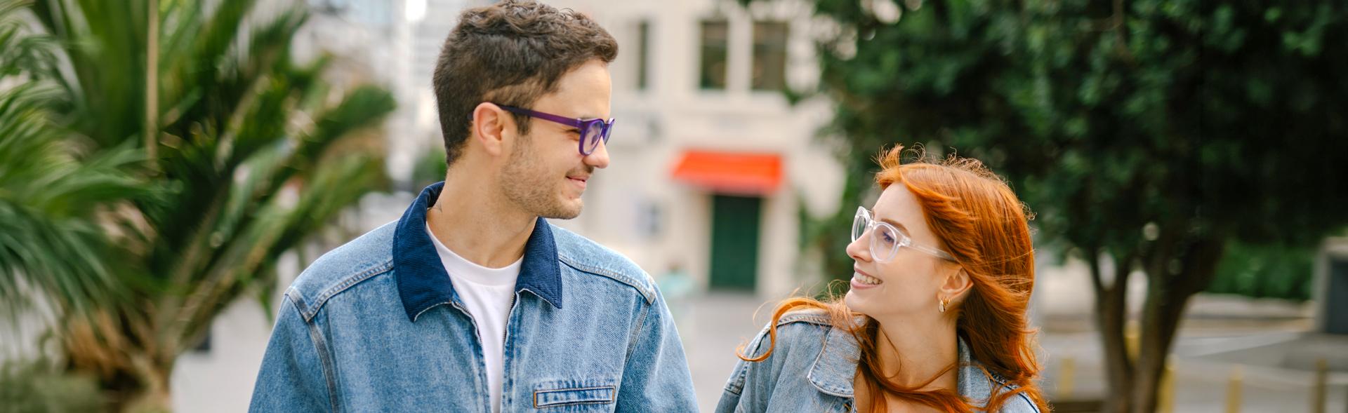 Couple wearing Dresden Vision Australia prescription glasses, smiling at each other outdoors, violet and clear frames