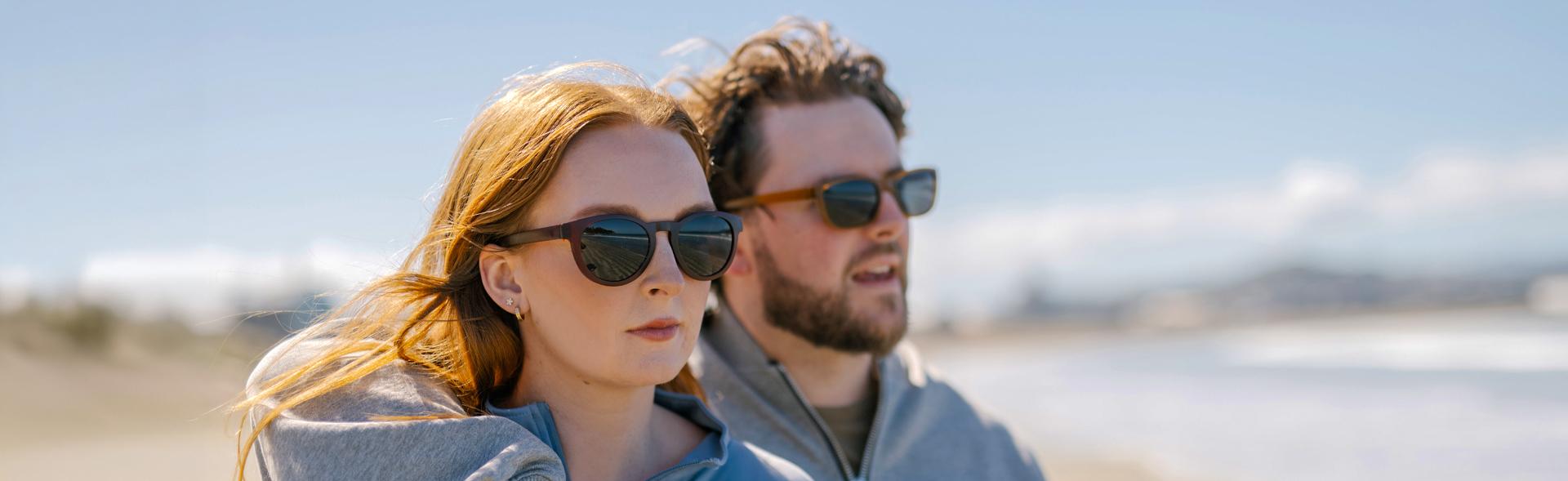 Couple wearing Dresden Vision prescription sunglasses outdoors, with wind and sunlight on a beach