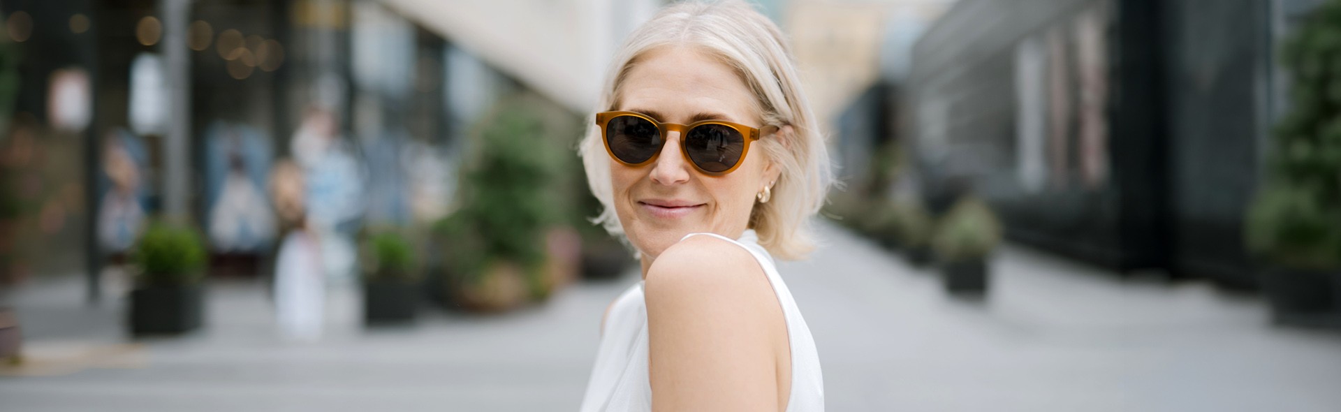 A woman outdoors wearing amber-framed Dresden Vision New Zealand multifocal sunglasses, created to provide sharp vision at near, intermediate, and far distances in bright sunlight.