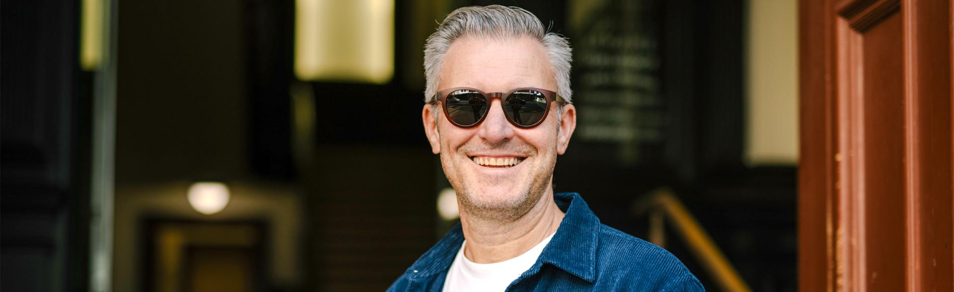 Man wearing Dresden Vision progressive sunglasses, smiling outdoors in a modern urban setting