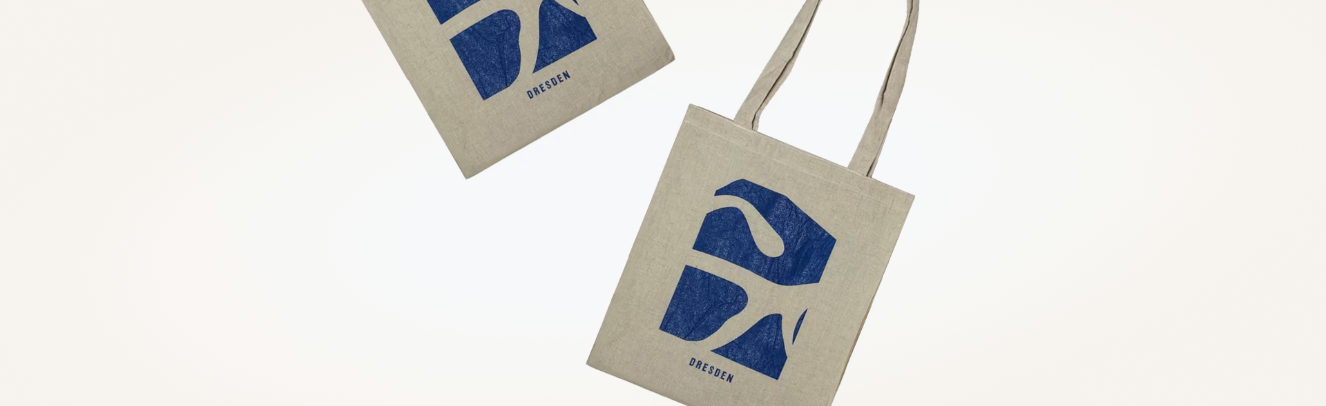 Two Dresden Vision canvas tote bags in beige with blue abstract designs and 'DRESDEN' printed, arranged diagonally on a white background.