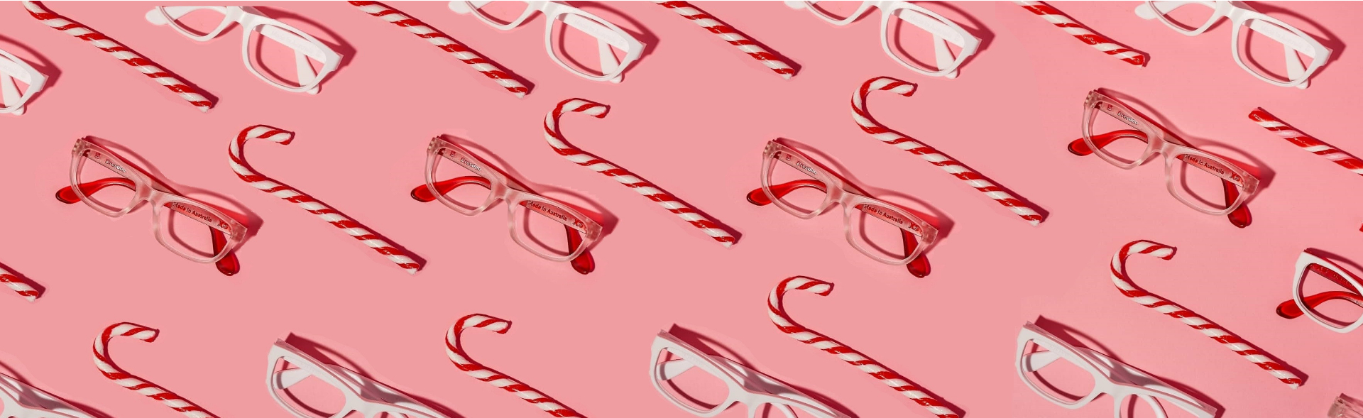 Red and white candy canes are placed diagonally alongside white and red eyeglasses on a pink background, highlighting festive-themed Christmas glasses in Australia with a playful and colourful design arrangement.